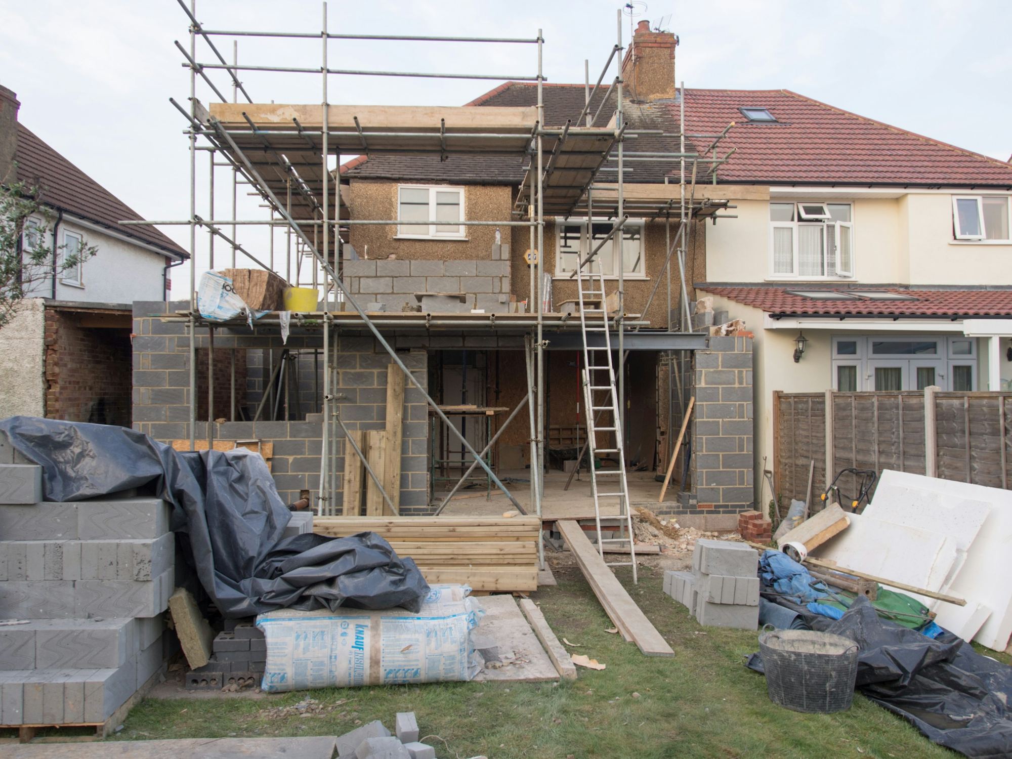 A two-storey rear extension under construction, wrapped in scaffolding with ladders